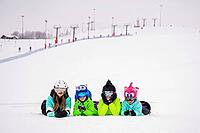 Group of children and teenagers lie in the snow at a ski resort. Ski lifts and skiers are visible in the background. The atmosphere is cheerful and carefree, emphasizing the joy of winter recreation [IBR125405008]
