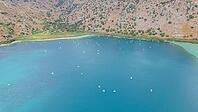 Kournas Lake at the foot of the mountains during peak tourist season, with many visitors enjoying pedal boats in clear sunny weather on Crete island [IBR125405080]