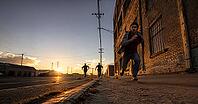 Men running down an urban street at sunset, with dramatic lighting and an industrial backdrop. Man on the run, fleeing from the police, AI generated [IBR125407386]