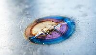 Close-up of temper color gradient bands radiating from a cooled weld point on a flat metal surface, straw to bronze to blue transition, heat affected zone, industrial macro photography, AI generated [IBR125407398]