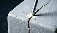Thin metallic lithium dendrite filament tip widening a narrow crack in a pale grey ceramic block, charcoal background, wedge expansion battery failure science, AI generated [IBR125407402]