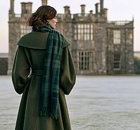 Back view of a woman in a forest green wool coat with a plaid scarf standing before a grand historic stone Scottish estate castle. AI generated [IBR125407407]