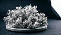 Dense diffuse cluster of fine metallic lithium dendrite filaments in a fluffy mossy formation on dark ceramic substrate, charcoal background, industrial lighting, battery failure science, AI generated [IBR125407422]