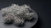 Dense diffuse cluster of fine metallic lithium dendrite filaments in a fluffy mossy formation on dark ceramic substrate, charcoal background, industrial lighting, battery failure science, AI generated [IBR125407430]