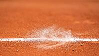 Fine white chalk dust suspended mid-air above a reddish-orange clay tennis court's boundary line, freshly disturbed mark below, bright daylight, decisive line call sports concept, AI generated [IBR125407432]