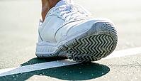 Close-up of a white tennis shoe's herringbone tread sole pressed against a hard court surface along a painted white baseline, bright natural daylight, sports footwork concept, AI generated [IBR125407446]