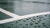 Scattered raindrops on a smooth dark green hard tennis court surface beside a faint white line, soft overcast daylight, no players visible, rain delay sports concept, AI generated [IBR125407462]