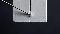 Thin metallic lithium dendrite filament tip widening a narrow crack in a pale grey ceramic block, charcoal background, wedge expansion battery failure science, AI generated [IBR125407465]