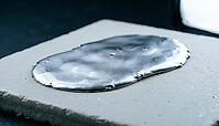 Smooth continuous metallic lithium deposition layer spreading laterally across a flat pale grey ceramic substrate, charcoal background, industrial lighting, high temperature battery science, AI generated [IBR125407470]