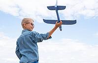 Happy child playing with a toy airplane against a blue sky in an open field [IBR125411094]