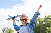 Happy child playing with a toy airplane against a blue sky in an open field [IBR125411099]