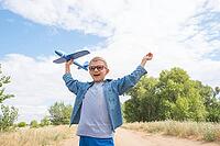 Portrait of a happy child playing with a toy airplane against a blue sky in an open field [IBR125411104]