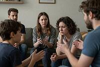 Emotional group therapy and psychological counseling during an intense family crisis discussion, interpersonal communication breakdown and mediation, concerned relatives sitting together in a living room circle, diverse generational perspectives clashing  [IBR125414127]