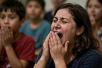 Collective trauma and raw human grief during a devastating crisis, intense emotional distress manifests through an agonizing scream of a weeping woman, hands clasped near her open mouth as tears stream down tightly shut eyes, overwhelming psychological sh [IBR125414131]