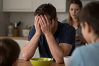 Mental breakdown and parental burnout of a desperate father sitting at breakfast table with family, emotional distress and severe anxiety overwhelm, psychological exhaustion clashes with domestic daily responsibilities, hands covering face depict chronic  [IBR125414132]