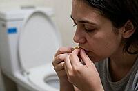 Young woman dealing with nausea, bulimia nervosa, morning sickness, medication intake and psychological distress next to an open ceramic toilet bowl, intimate moment of vulnerability reflecting somatization disorders and gastrointestinal pain, physiologic [IBR125414136]