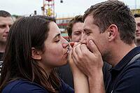 Intimate sensory connection and youth subculture during public celebration, young couple sharing breath through clasped hands in a crowd, peer group dynamics and emotional vulnerability amidst amusement park structures, closed eyes expressing profound mut [IBR125414138]