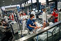 Emergency room healthcare crisis in intensive medical care, dedicated nurse comforts elderly patient on hospital bed during critical triage situation, frantic clinical environment full of paramedics and doctors managing severe overload in clinical hallway [IBR125414146]