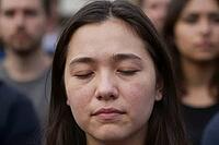 Collective mourning and silent protest during public remembrance, focused young woman with closed eyes amidst gathered crowd sharing grief, somber expression and introspective meditation representing empathy within civil society, peaceful assembly uniting [IBR125414149]