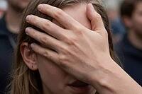 Psychological stress, sensory overload, mental exhaustion and anonymity in public crowds, an individual shielding the eyes with a tense hand across the face, tactile gesture of social anxiety, emotional withdrawal, shame, migraine pain, cognitive fatigue, [IBR125414150]