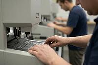 Precision manufacturing and vocational engineering workflows in modern laboratory facilities, skilled technicians operate complex control panels of industrial calibration machinery, tactile manual labor merges with automated high tech processing to optimi [IBR125414153]