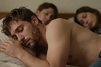 Shirtless young man sleeping peacefully on a pillow in bed beside companions, intimate morning rest, shared domestic vulnerabilities in cozy bedroom, tranquil somatic regeneration of exhausted youth after long night, blurred background figures resting tog [IBR125414164]