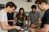 Collaborative teamwork and cognitive problem solving in shared living space, young adults assembling colorful puzzle pieces on kitchen counter, integrating collective intelligence for complex task management, strategic alignment and synergy in flatshare c [IBR125414173]
