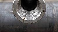 Head-on view of a threaded steel pipe joint opening with a fine crack radiating from the rim, circular thread geometry, industrial macro photography, structural failure investigation, AI generated [IBR125414175]