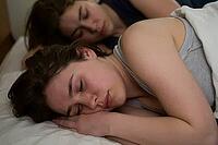 Deep restorative sleep of two young women in bed, somatic recovery through peaceful intimacy and neurological rest during circadian regeneration phases, closed eyes showing vulnerability and interpersonal trust in private domestic space, relaxed facial ex [IBR125414186]
