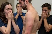 Vulnerable shirtless man experiencing collective shock, social stigma and intense emotional distress surrounded by stunned gasping companions, somatic expression of sudden trauma and exposure, psychological confrontation within an interpersonal group sett [IBR125414187]