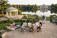 Plein air landscape painting, cultural heritage tourism, peaceful picnic leisure by lake, neoclassical palace architecture reflection in water, aspiring artists capturing serene botanical vistas on wooden easels, a young couple reading literature together [IBR125414188]