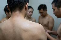 Somatic vulnerability, collective exposure and human intimacy in an enclosed communal environment, young adults standing together with bare skin, close physical proximity creating intense social tension and emotional bonding, the tactile warmth of bare sh [IBR125414191]