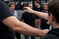 Interpersonal conflict, group dynamics, nonverbal communication in urban spaces, physical gestures, outstretched arms frame tense social interactions among young men gathered near a transit vehicle, intense body language and defensive posture serve as a v [IBR125414193]