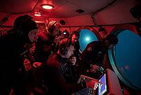 Deep sea underwater exploration crew inside submarine cockpit with sonar navigation monitoring, marine research team in diving suits analyzing bathymetric charts, circular porthole windows revealing dark ocean water illuminated by external submersible spo [IBR125414196]