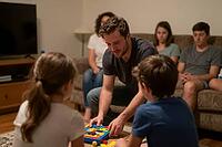 Cognitive development and family bonding during educational board games in a living room, an adult mentor guides children with tactile logic puzzles, fostering spatial thinking and cooperative learning through haptic playful interaction, relatives observe [IBR125414198]