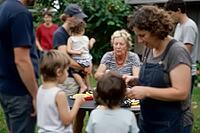 Intergenerational family cohesion and informal care economy in an outdoor domestic garden, diverse generations assemble around a shared table, grandparents alongside parents and young offspring establish social continuity, informal childcare networks mani [IBR125414216]