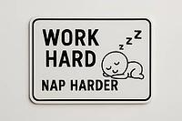 White sign with black text Work Hard Nap Harder and a sleeping cartoon character, emphasizing the importance of rest for productivity, AI generated [IBR125421189]