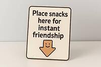 Humorous sign suggests placing snacks for instant friendship, featuring a downward arrow with a smiley face, AI generated [IBR125421201]