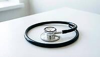 Coiled stainless steel stethoscope with black rubber tubing on a plain white clinical countertop, cardiac monitoring equipment, soft natural daylight, studio photography, AI generated [IBR125421219]