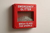 Red emergency glitter box hanging on a bright white wall, poised for breaking and unleashing a shower of sparkling brilliance, AI generated [IBR125421224]