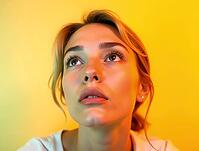 Close-up portrait of young woman looking up with hope and faith on a vibrant yellow background, AI generated [IBR125421232]