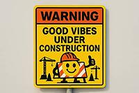 Yellow warning sign displaying good vibes under construction with a smiling face, cranes and traffic cones, conveying positivity and optimism during building works, AI generated [IBR125421246]