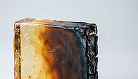 Close-up of translucent amber epoxy resin edge showing thermal degradation gradient from clear to charred, semiconductor materials science macro photography, thermal endurance concept, AI generated [IBR125421252]