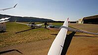 People working on gliders in an open field near a hangar under a bright sky, Aérodrome de Château-Arnoux - Saint-Auban, France [IBR125421618]