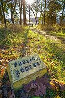 A public access sign along a sunlit forest path, surrounded by trees and fallen leaves, creating a tranquil natural setting. A marker denoting public access next to a walking path, Gabriola Island, British Columbia, Canada [IBR125421633]