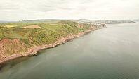 Panoramic view of cliffs and water with rolling fields stretching into the distance, - Drone photography - South coast of Devon, England, UK [IBR125421670]