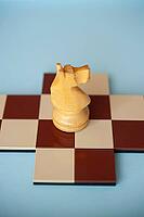 A yellow wooden knight shaped like a horse on a brown and beige chessboard [IBR125424484]