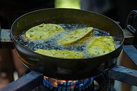 Golden brown fritters sizzle and bubble as they cook in a dark metal pan filled with bubbling hot oil over a blue gas flame, Bridal Falls, Rosedale BC Canada [IBR125424485]
