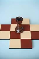 A dark wooden rook on a brown and beige chessboard with a light blue background [IBR125424498]