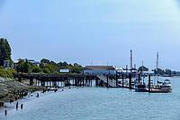 A scenic view of a waterfront with various boats moored to a wooden pier and industrial structures lining the shore, Richmond Whistler, BC, Canada [IBR125424500]